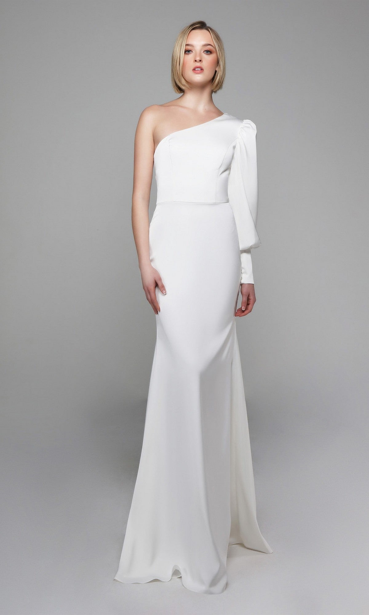 Woman in the Alyce 7065 Long White Dress, featuring an ivory fitted silhouette with a single long sleeve and one-shoulder design, standing against a plain light gray background.